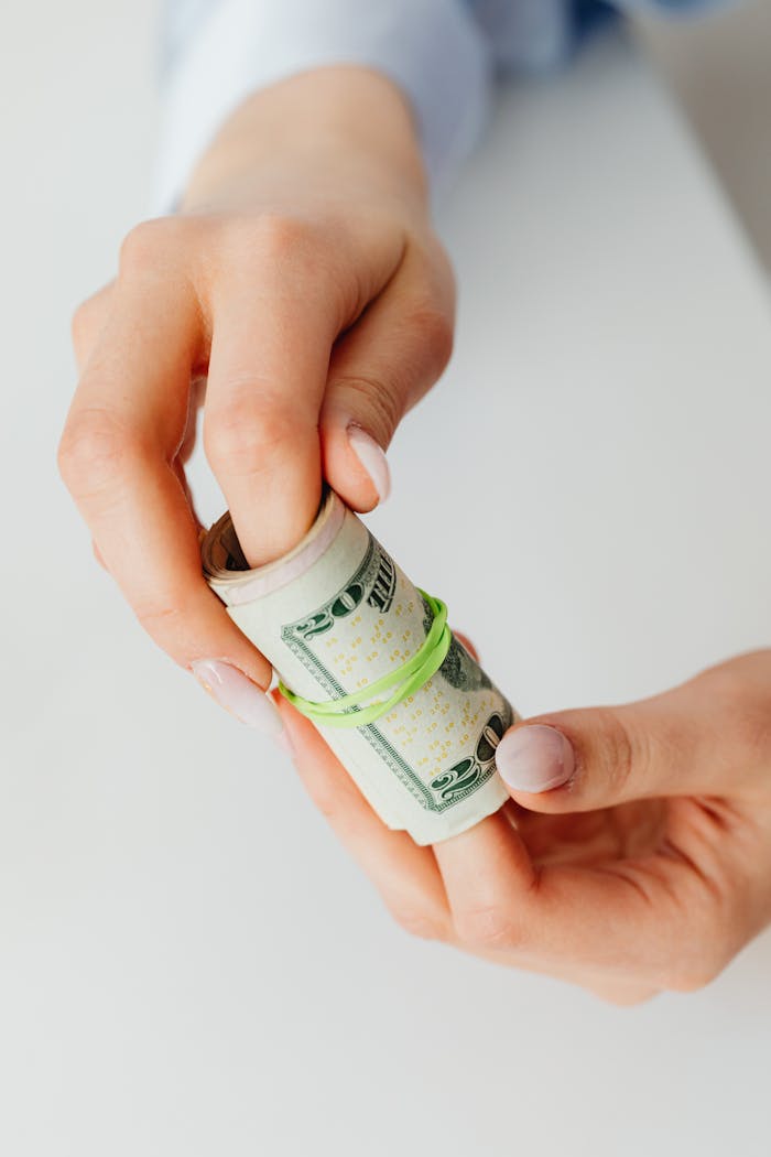Mastering the First Impression: Your intriguing post title goes here Hands holding a rolled bundle of US dollar bills bound by a rubber band, in a bright setting.
